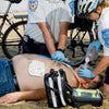 Person receiving CPR on a beach with emergency responders and medical equipment.