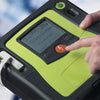 Hand pressing a button on a green and black electronic device with a digital display.