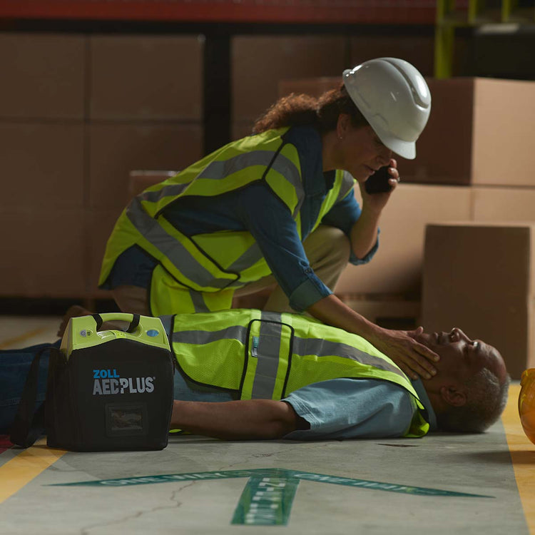 Person performing CPR on a mannequin with a ZOLL AED Plus defibrillator nearby.