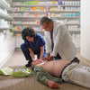 Two people performing CPR on a mannequin in a pharmacy setting.
