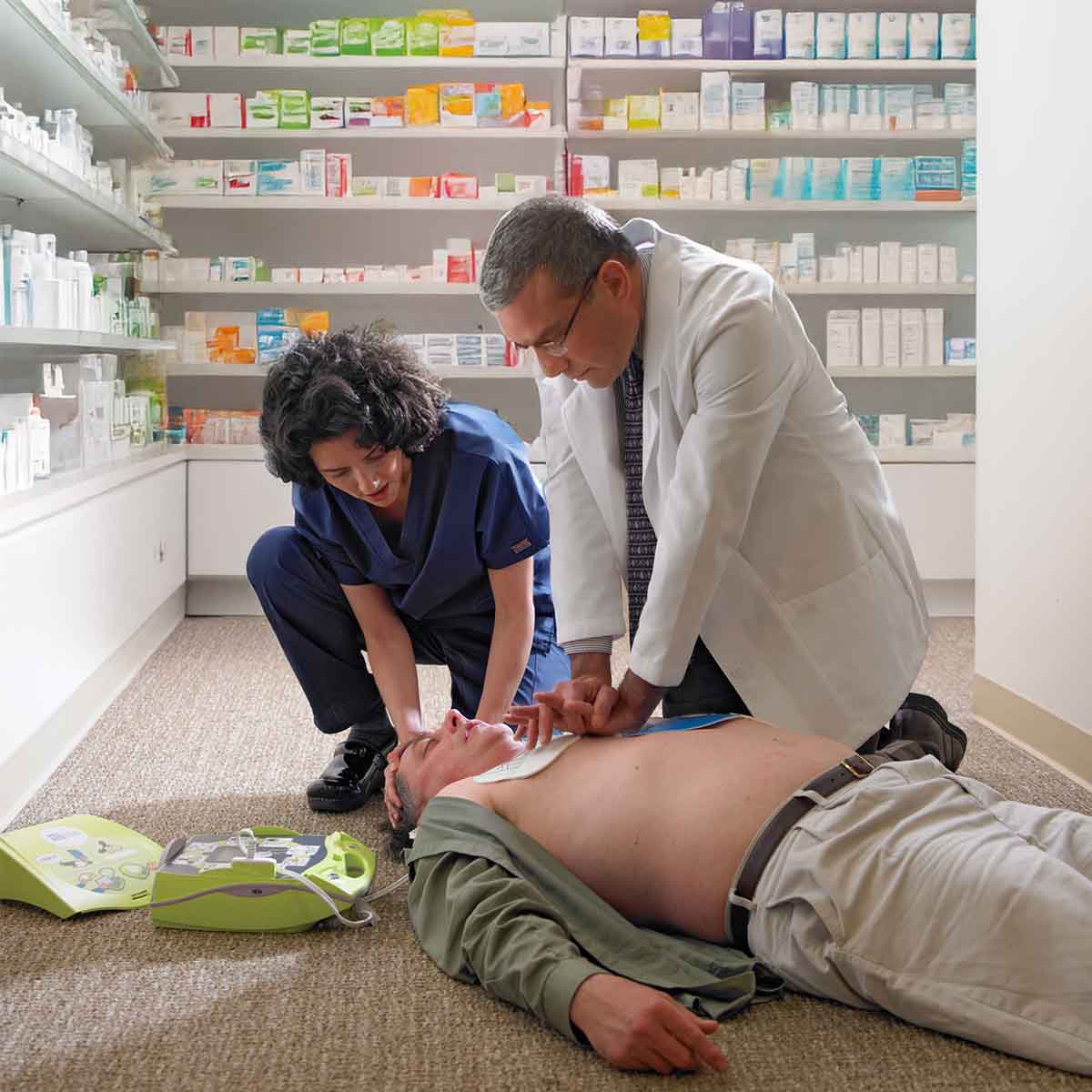 Two people performing CPR on a mannequin in a pharmacy setting.