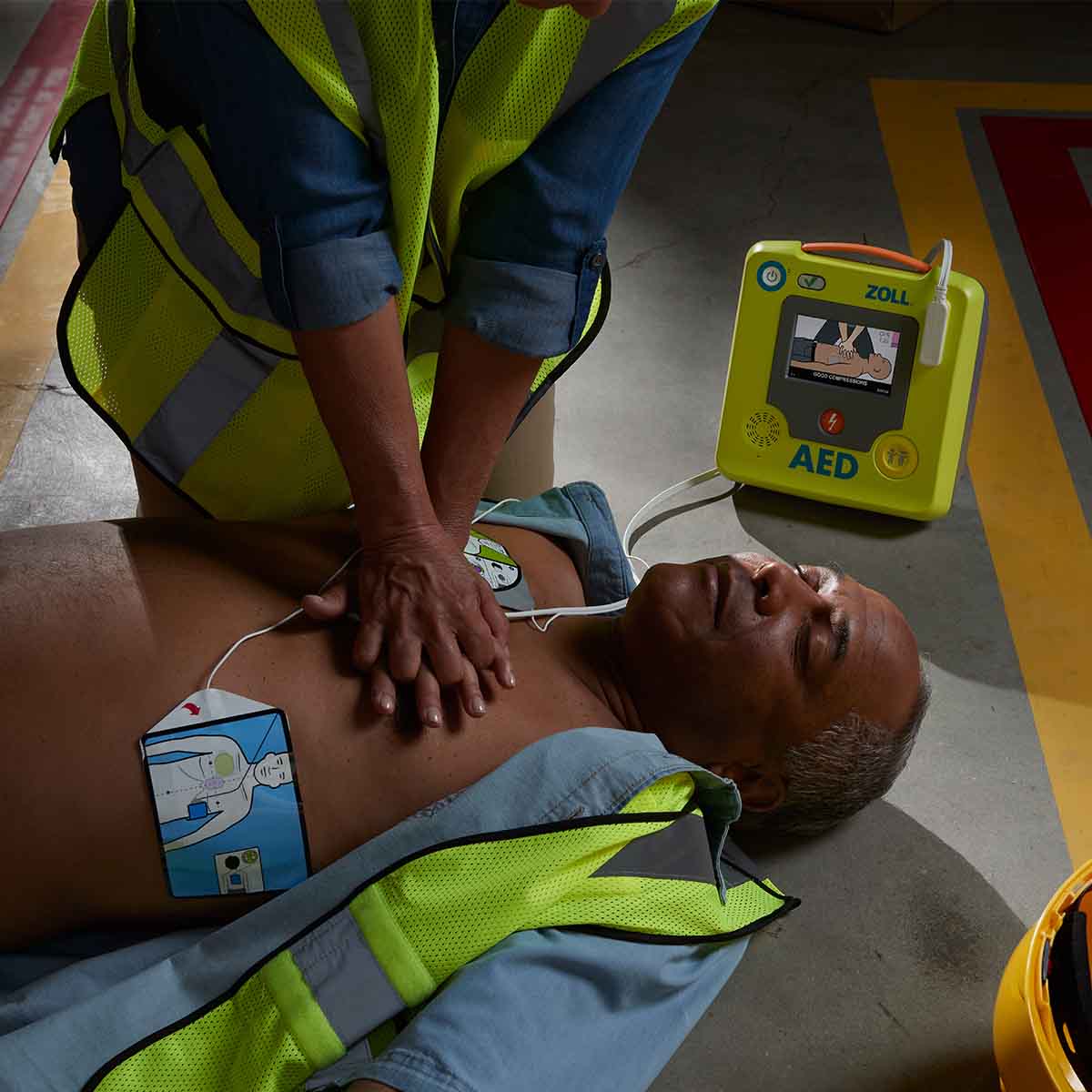 Person performing CPR on a mannequin with an AED device nearby.