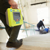 Person holding a Zoll AED in an indoor setting with blurred background