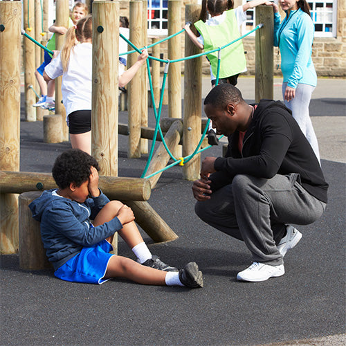 a small holding head in hands and cradling  knee in a school playground