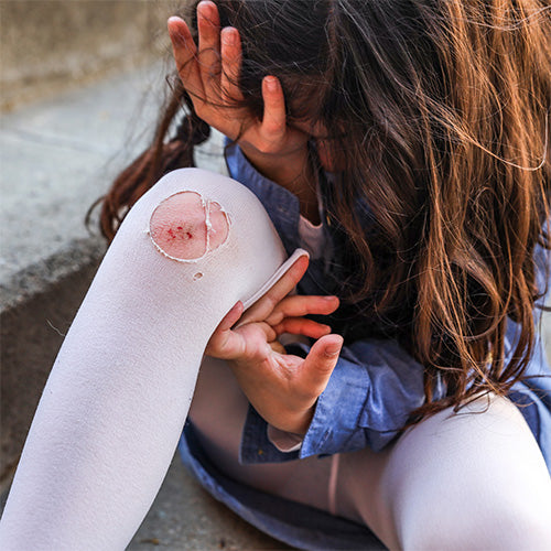A small child with a cut grazed knee with a hole in her tights