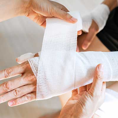 Person applying white bandage to another person's arm