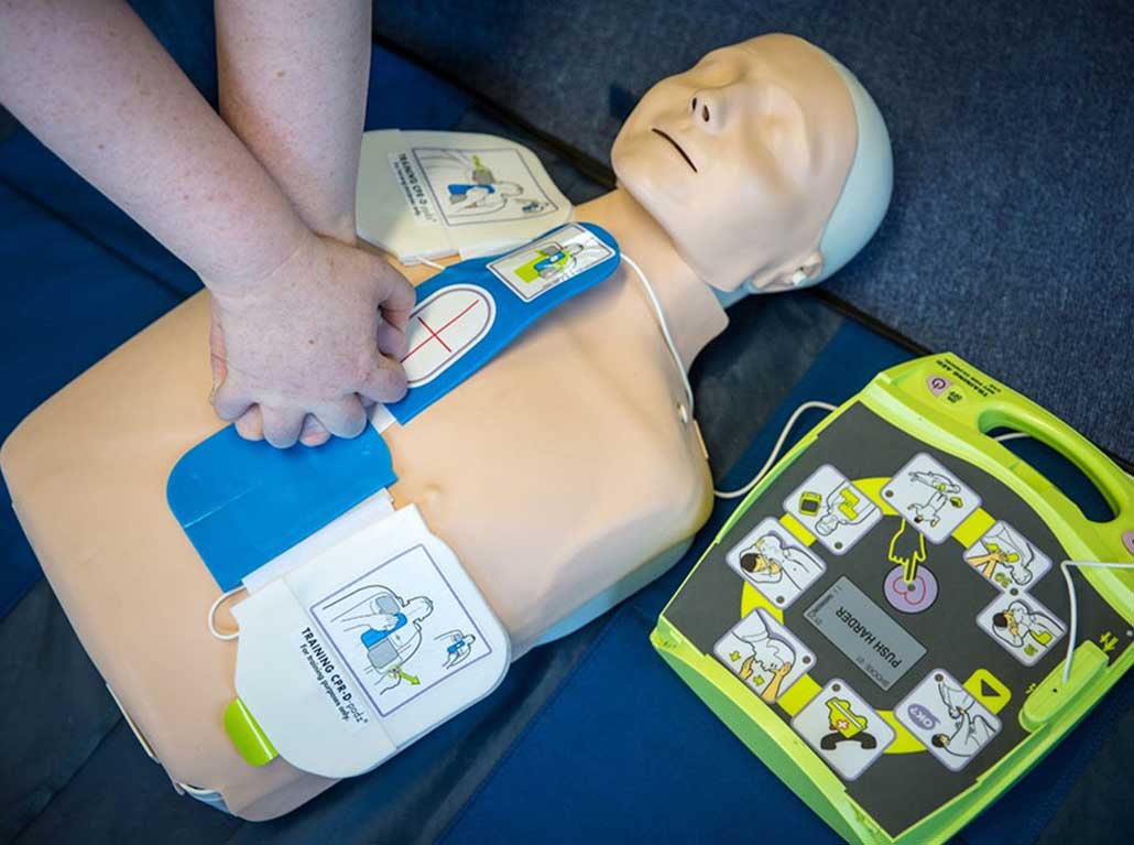 CPR training mannequin with AED monitor on a blue surface