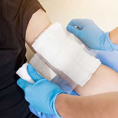 Person applying bandage to another person's arm with blue gloves