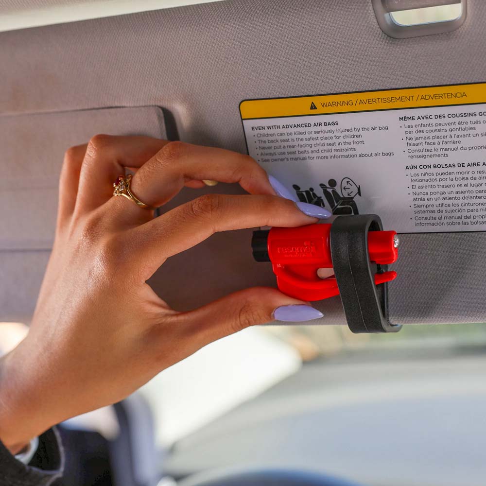 A woman securing a ResQMe 2-in-1 Rescue Tool to her car's sun visor.