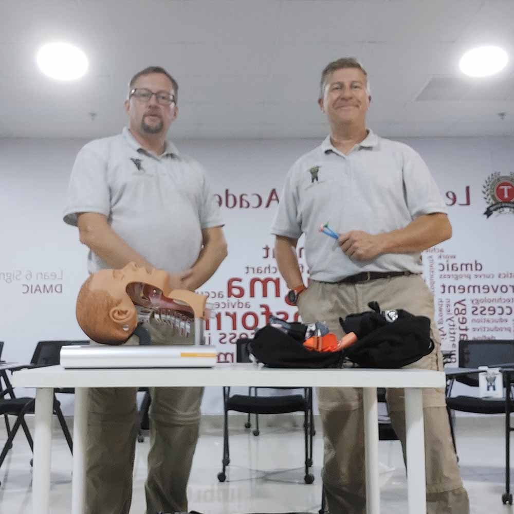 Two trainers in a classroom with their equipment on a desk, as part of a First Aid and Specialist Trauma (FAST) course.