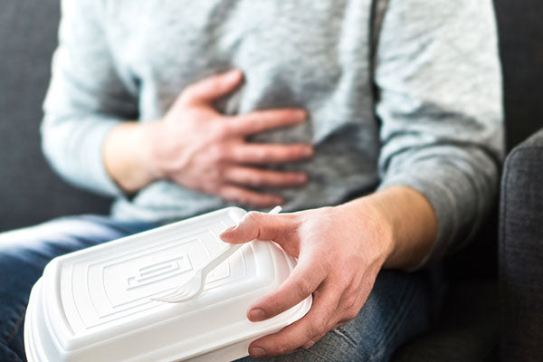 A person sitting on the couch with a takeaway box in their left hand, and their right hand on their stomach.