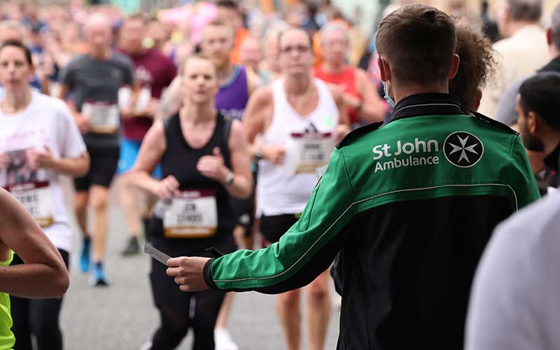 Person in a St John Ambulance jacket among runners at a race
