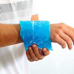 Person applying a blue gel pack to their wrist on a white background