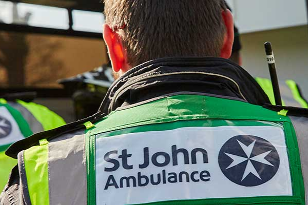 Person wearing a St John Ambulance vest in front of an ambulance.