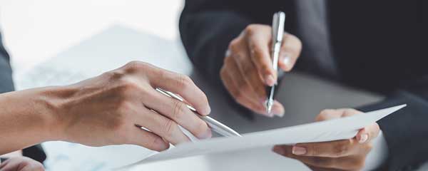 Two people signing a document with pens in a close-up shot.