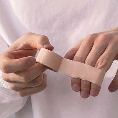 Person holding a roll of beige elastic bandage against a white background