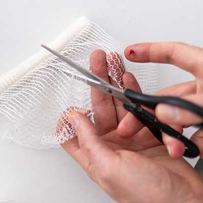 Person cutting a piece of gauze with scissors on a white background